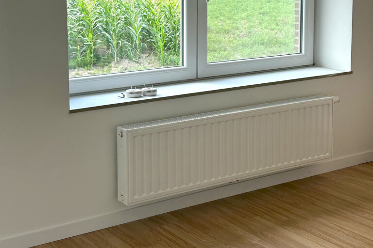 Witte radiator onder venster met uitzicht op groen veld geïnstalleerd door Degryse Projects