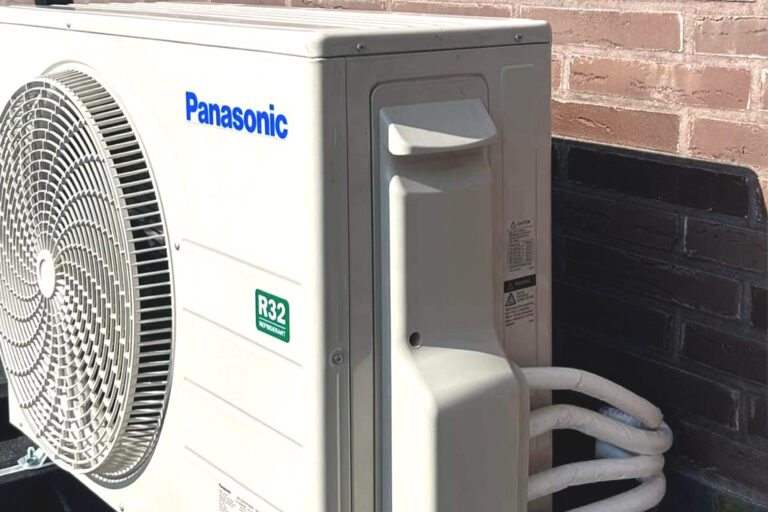 Zijaanzicht van een Panasonic airconditioning buitenunit geïnstalleerd naast een bakstenen gebouw.